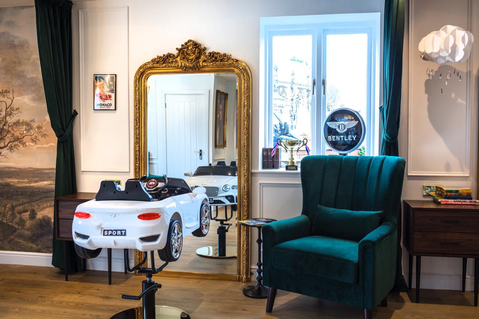A car-shaped salon chair beside a gold mirror.
